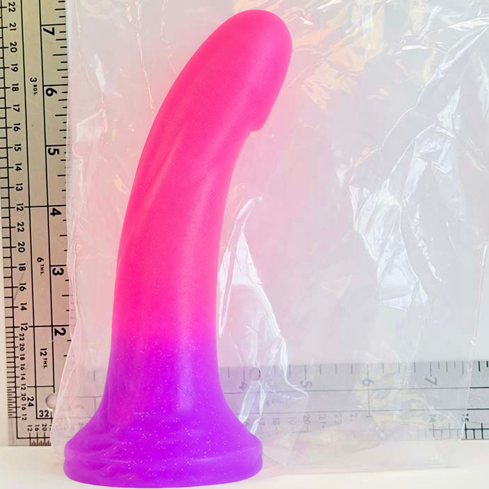 A pink and purple gradient silicone adult novelty product standing upright next to a plastic bag and ruler for scale.